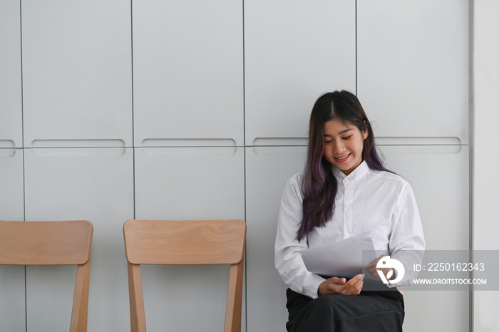 Smiling woman holding resume and waiting for interview.