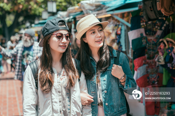 two happy asian female people walking at green outdoor mexico market in los angeles. joyful curious 