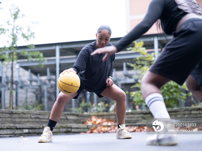 Two female friends playing basketball outdoors