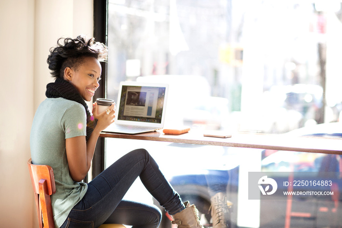 Smiling young woman using laptop in cafe