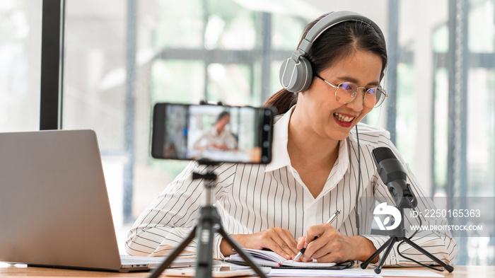 Asian women podcaster podcasting and recording online talk show at studio using headphones, professi