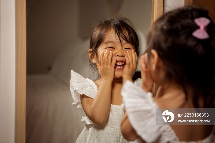 Smiling little girl looking in mirror at home