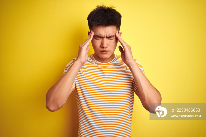 Young asian chinese man wearing t-shirt standing over isolated yellow background with hand on head f