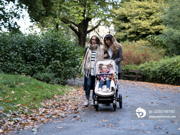 Lesbian couple walking with baby in park at autumn�