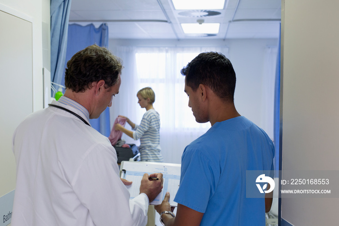 Male doctors discussing medical chart in hospital room doorway