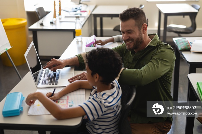 Young school teacher helping boy with study on laptop in