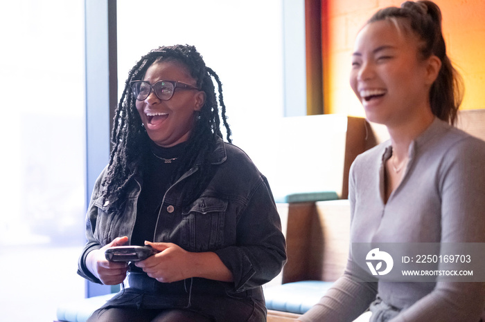 Female friends having fun while playing in video games at pub