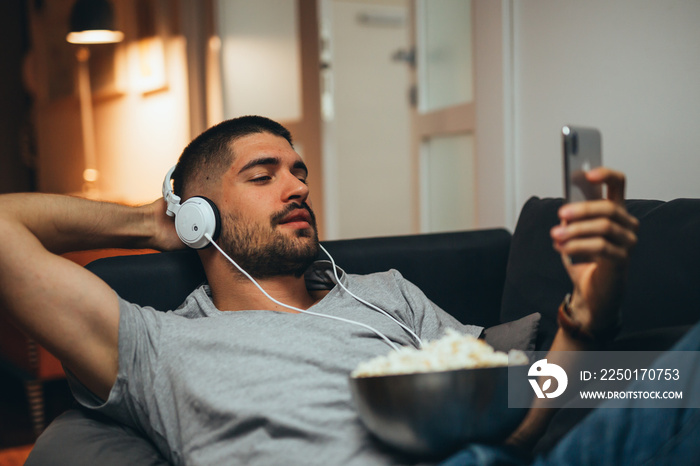 man using mobile phone relaxed in sofa at home listening to a music