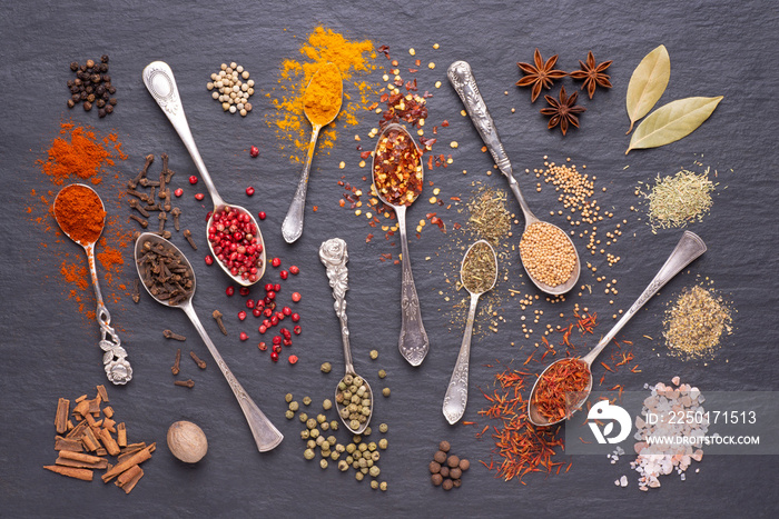 Herbs and spices in silver spoons on black stone background