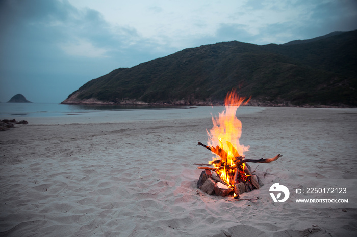 Horizontal outdoors shot of blazing campfire on sand at the seaside.