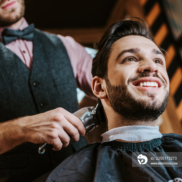 low angle view of barber holding trimmer while styling hair of happy man in barbershop