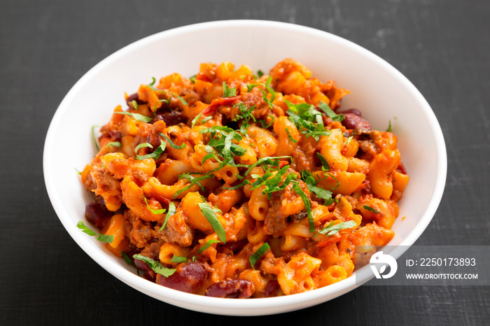 Homemade Chili Mac and Cheese with Parsley in a white bowl over black background, low angle view. Cl