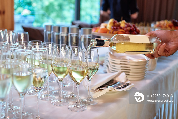 Waiter pours wine into wineglass at wedding reception, copy space. Sparkling glassware with wine and