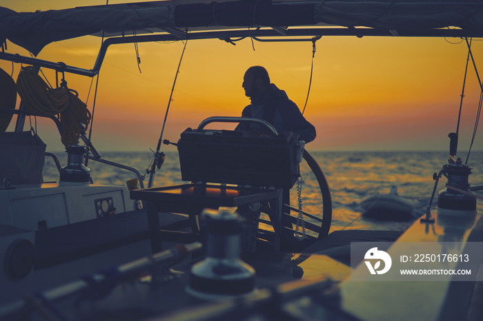 Sailor steering sailing boat with a rudder in dawn / twilight time on tje open sea.