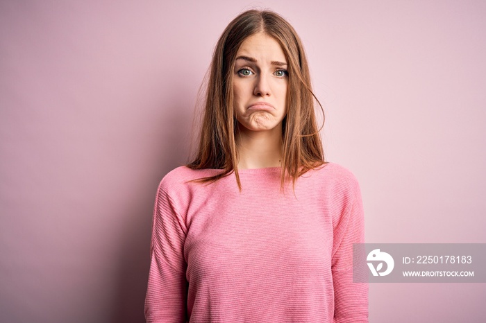 Young beautiful redhead woman wearing casual sweater over isolated pink background depressed and wor