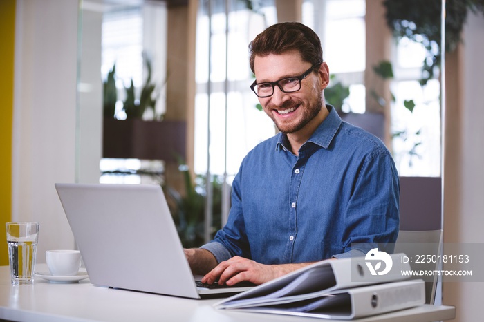 Portrait of cheerful businessman using laptop