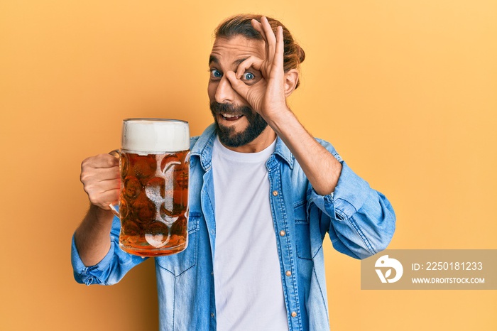 Attractive man with long hair and beard drinking a pint of beer smiling happy doing ok sign with han