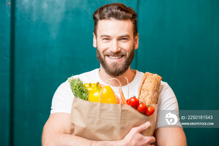 Handsome man holding a paper bag full of healthy food on the green background