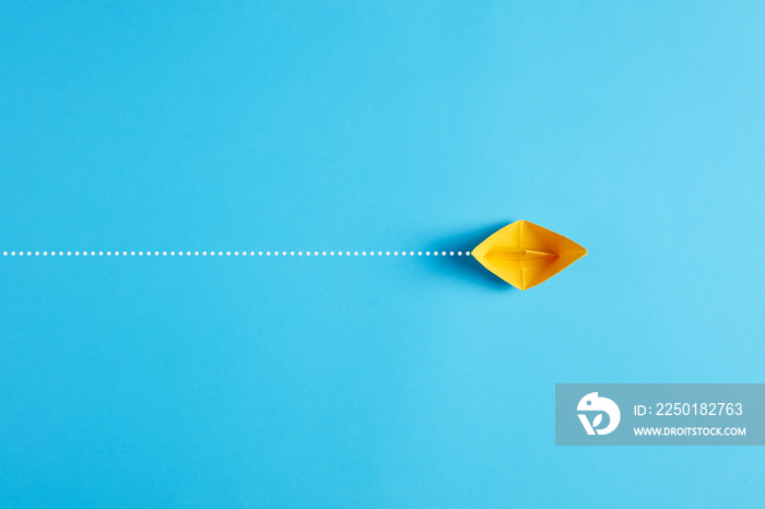 Yellow origami paper ship floats across the blue background