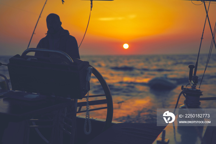 Sailor using wheel to steer rudder on a sailing boat.