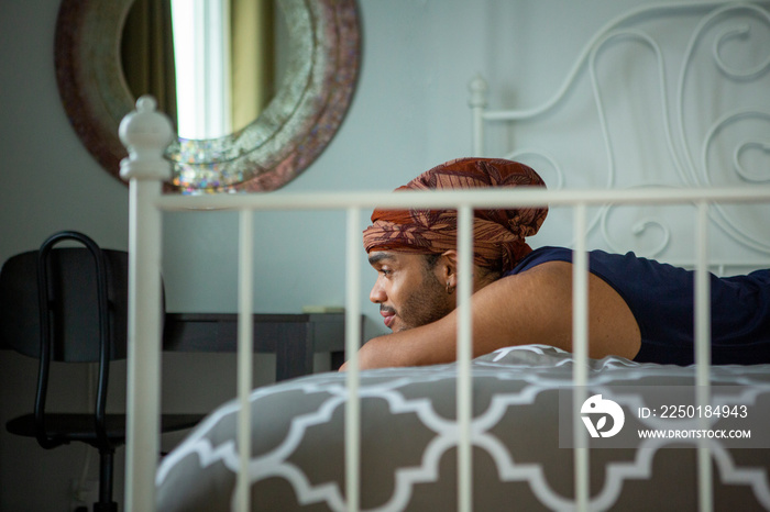 Side view of smiling young man lying on bed at home