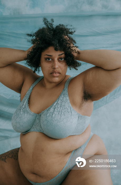 close up portrait of a plus size afro indigenous person looking at camera with hands in afro