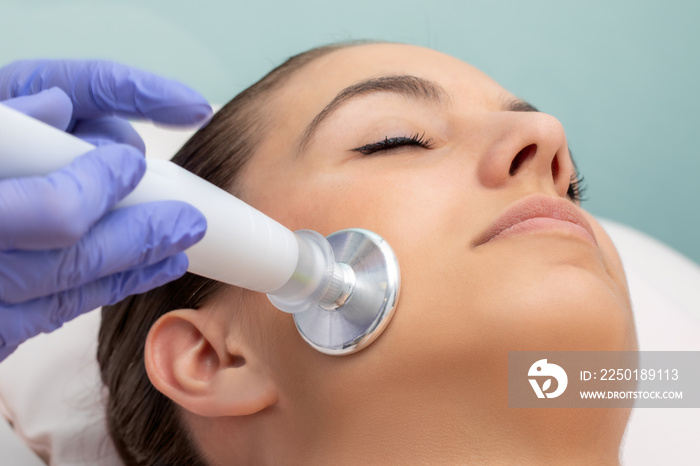 Therapist doing acne treatment with plasma lift technology on female face.