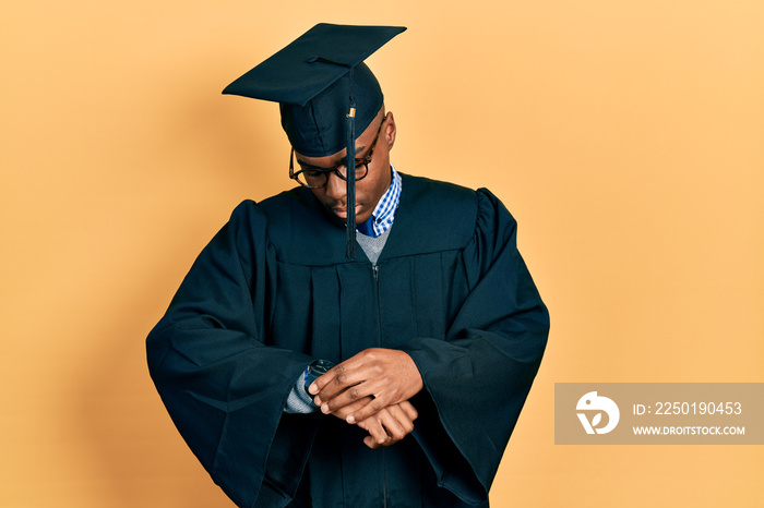 Young african american man wearing graduation cap and ceremony robe checking the time on wrist watch