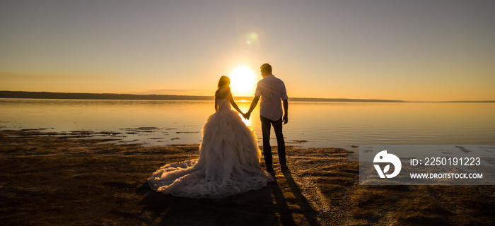 海边看日落的新婚夫妇。阳光明媚的夏季照片。新娘头发朝下。