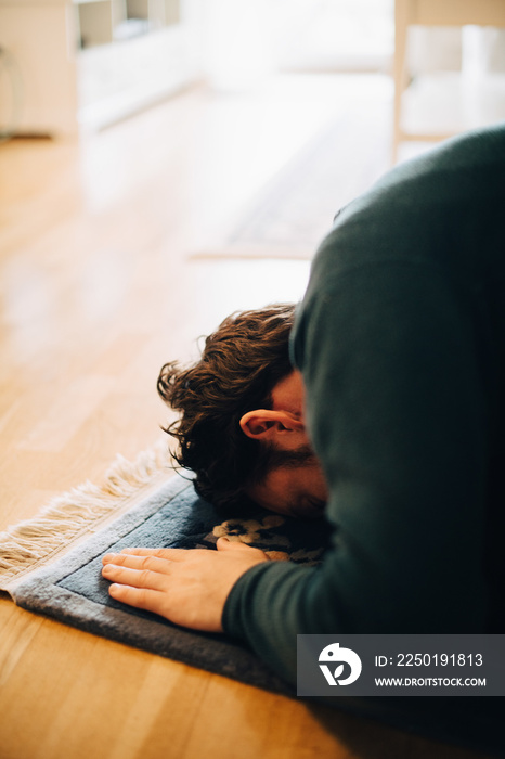 Close-up of man praying while bending on carpet in living room at home