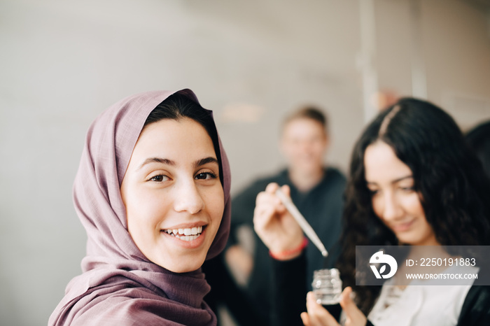 Portrait of smiling teenager in hijab learning with classmates in chemistry class