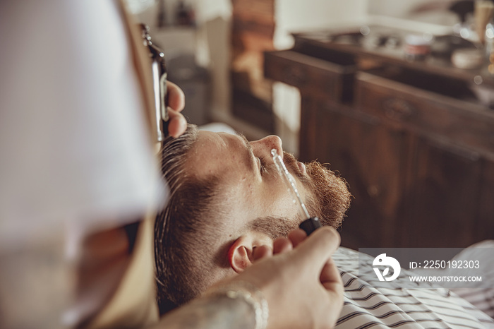 The barber applies the beard oil with a dropper. Photo in vintage style