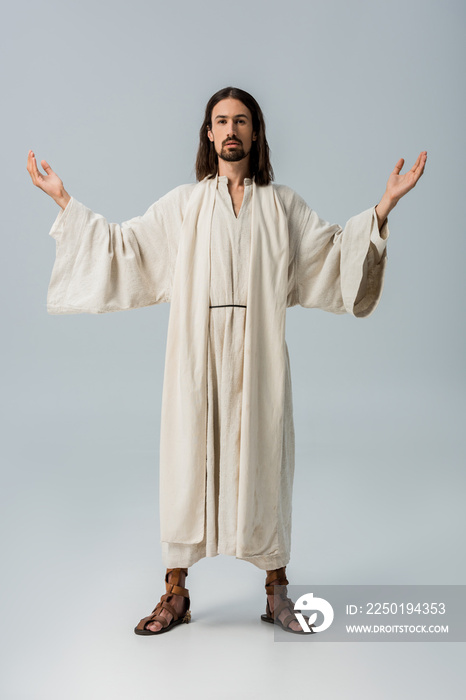 bearded man in jesus robe standing with outstretched hands on grey