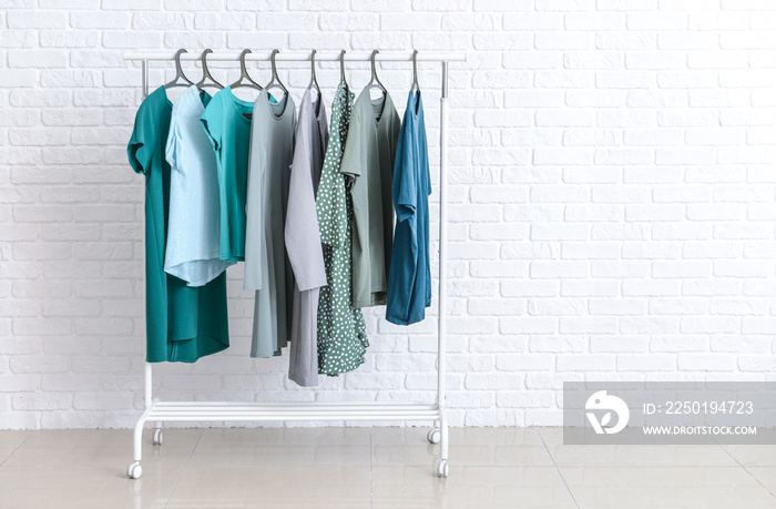 Rack with clothes after dry-cleaning near white brick wall