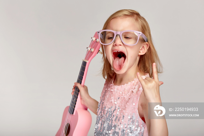 摇滚音乐概念。可爱的白人小女孩穿着亮粉色连衣裙露出舌头，