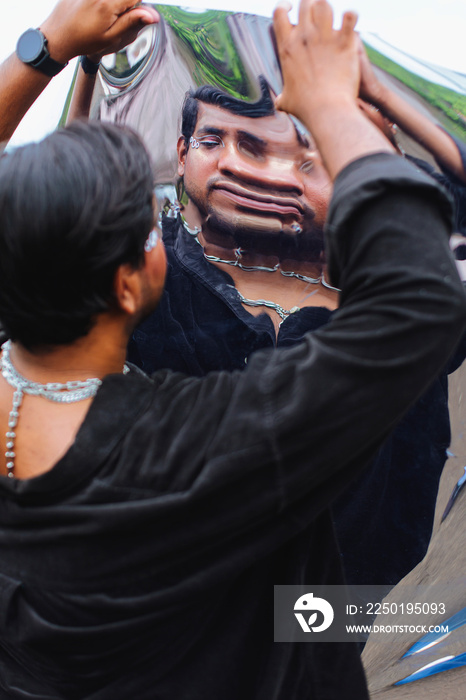 portrait of dark skinned Indian man looking into a distorted mirror