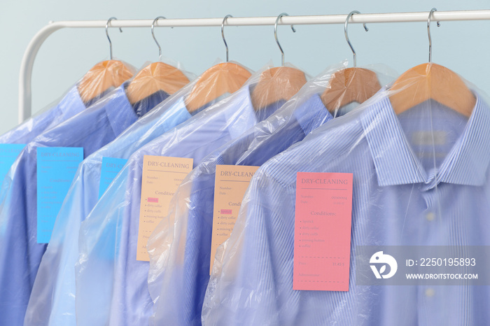 Rack with clothes after dry-cleaning on light background