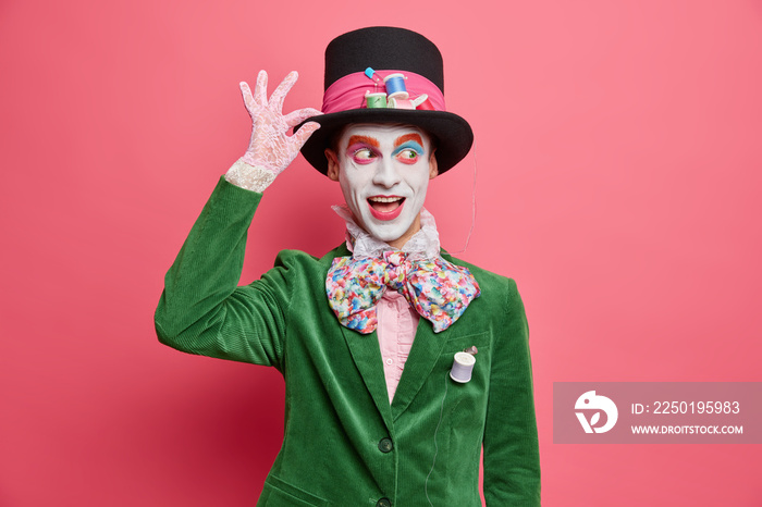 Positive insane hatter wears bright makeup ready for street performance or masquerade dressed in gre