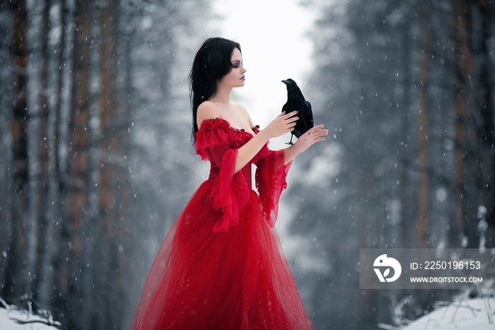 Woman witch in red dress and with raven in her hands in snowy fo