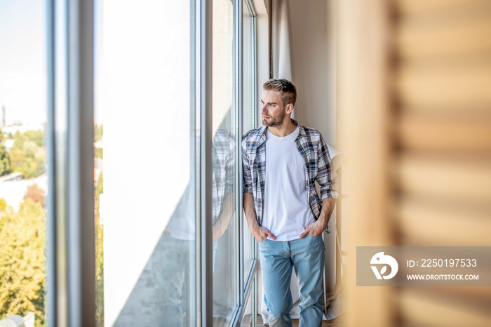 Young man in a checkered shirt looking out of the window