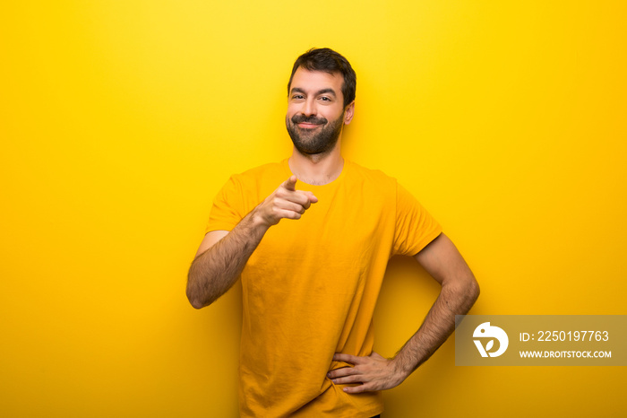 Man on isolated vibrant yellow color points finger at you with a confident expression