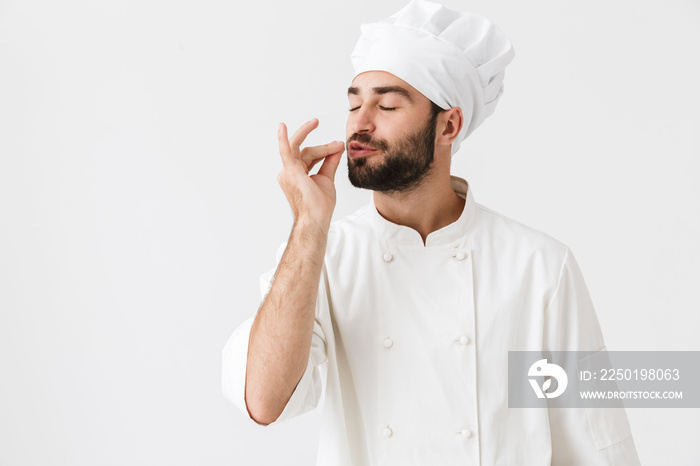 年轻的厨师穿着制服，在白墙背景上独自摆出姿势，做出美味的手势。