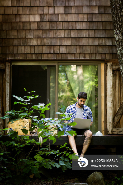 Young man using laptop outside cabin