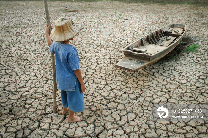 Boy looking to wooden boat on cracked earth.