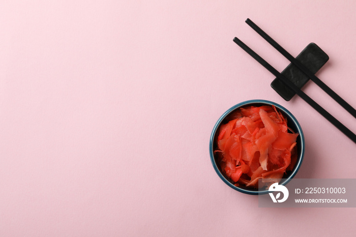 Bowl with red pickled ginger and chopsticks on pink background