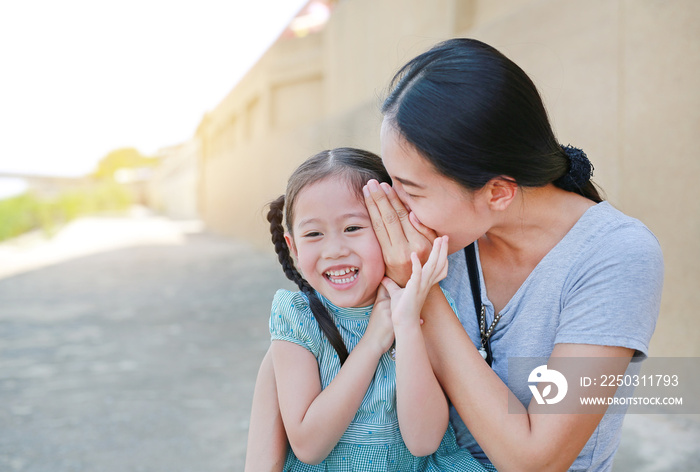 Happy mom whispering a something secret to her little daughter ear. Mother and kid communication con