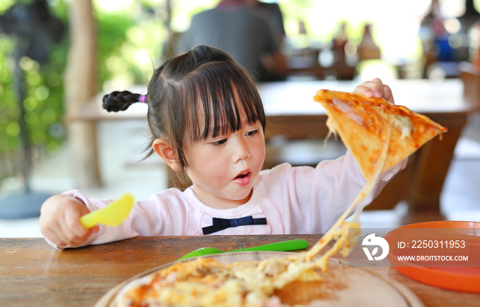 Little child girl eating pizza with funny face.