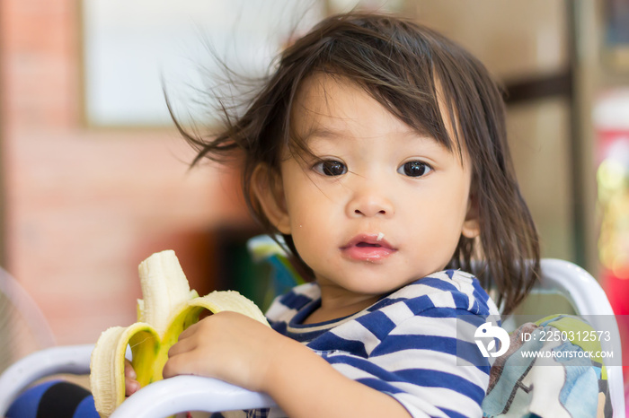 Portrait image of baby 1-2 years old. Happy Asian child girl enjoy eating a banana with sweet smilin