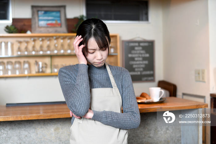 カフェ（飲食店）で悩むエプロン姿のアジア人の女性店員