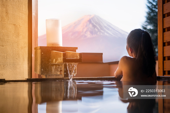 Beautiful woman enjoy onsen (mineral hot bath) in morning and seeing view of Fuji mountain in japan